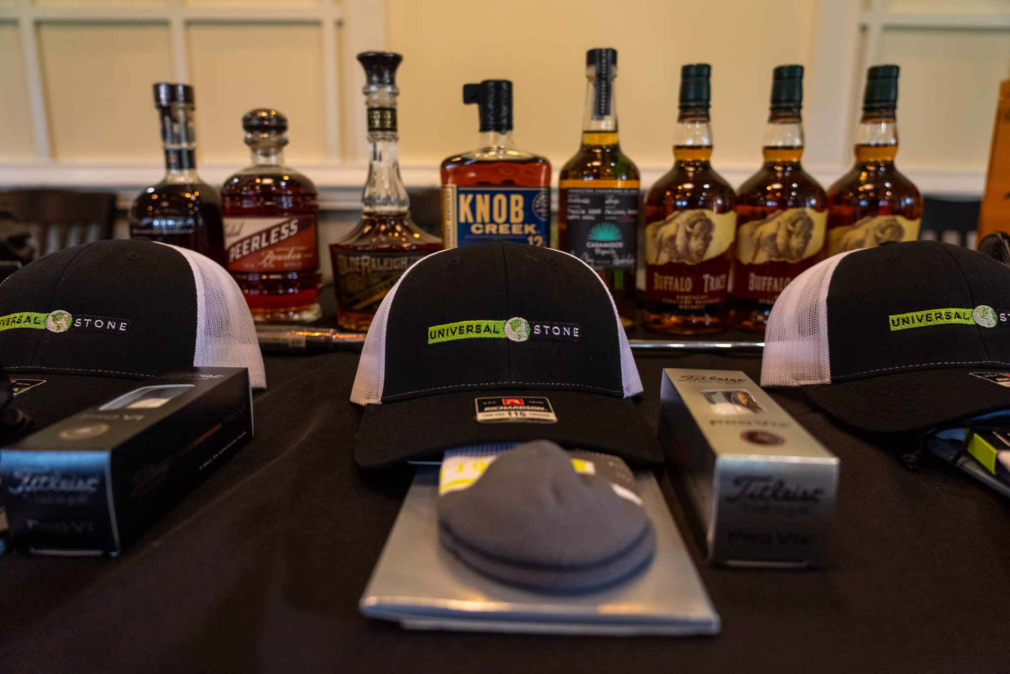 Prize-table still life — Universal Stone hats, Titleist Pro V1, premium bottles